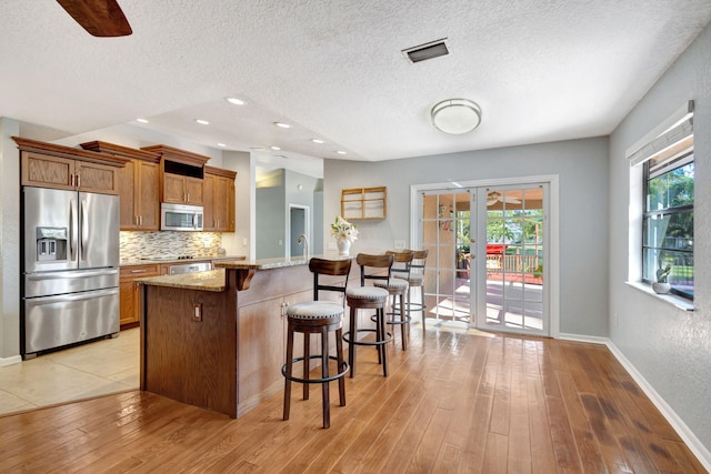 kitchen with light wood-type flooring, stainless steel appliances, light stone counters, and a breakfast bar area