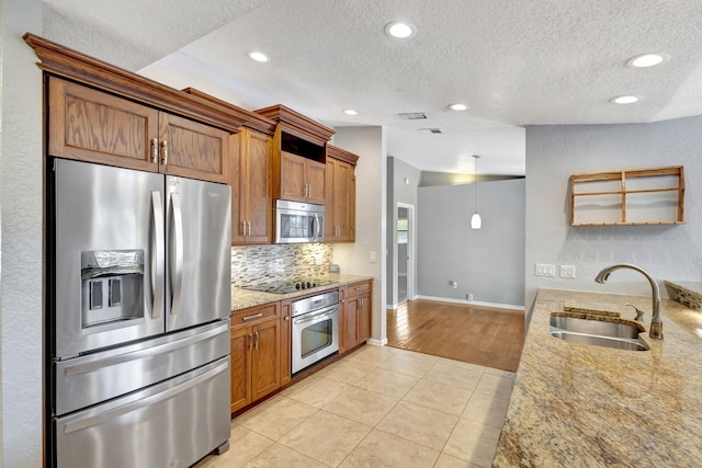 kitchen with light stone countertops, appliances with stainless steel finishes, a textured ceiling, sink, and light tile patterned flooring