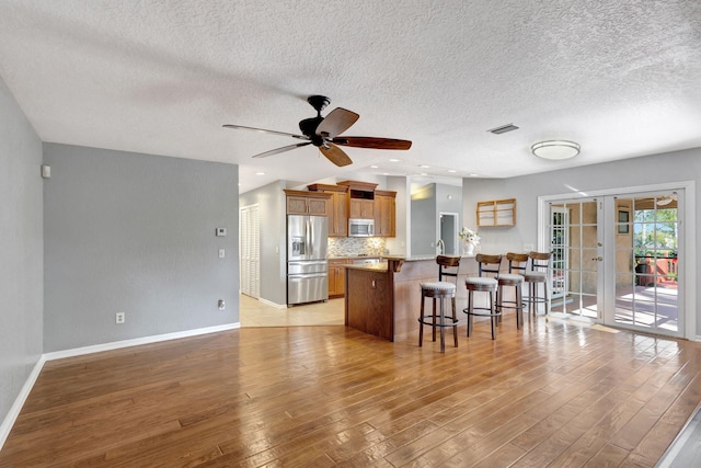 kitchen featuring decorative backsplash, a breakfast bar, a textured ceiling, stainless steel appliances, and light hardwood / wood-style flooring