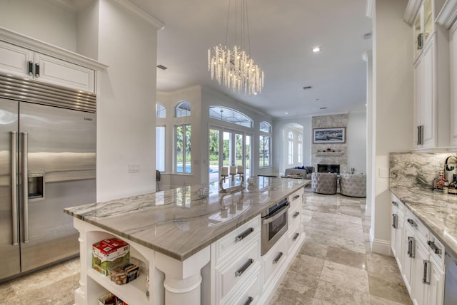 kitchen featuring light stone countertops, a fireplace, ornamental molding, white cabinetry, and stainless steel appliances