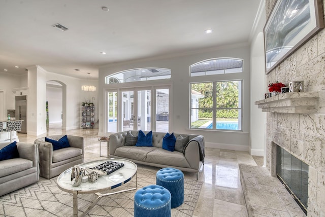 living room featuring a stone fireplace, crown molding, and french doors