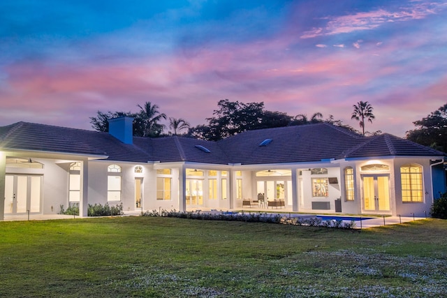 back house at dusk with a lawn, french doors, and a swimming pool