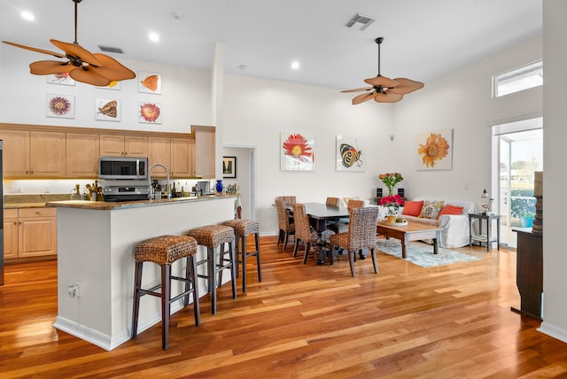 kitchen featuring a kitchen bar, stainless steel appliances, a high ceiling, and light hardwood / wood-style floors