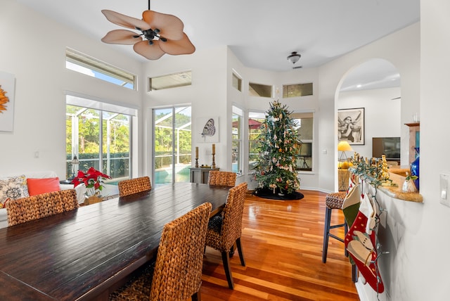 dining room with wood-type flooring, ceiling fan, and a high ceiling