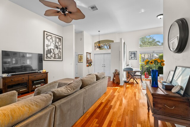 living room with a towering ceiling, ceiling fan with notable chandelier, and light wood-type flooring