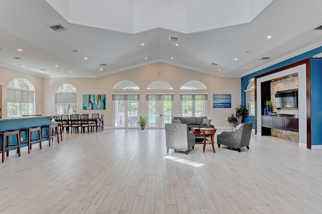 living room featuring lofted ceiling, light wood-type flooring, french doors, and crown molding