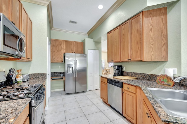 kitchen featuring dark stone counters, ornamental molding, stainless steel appliances, sink, and light tile patterned flooring