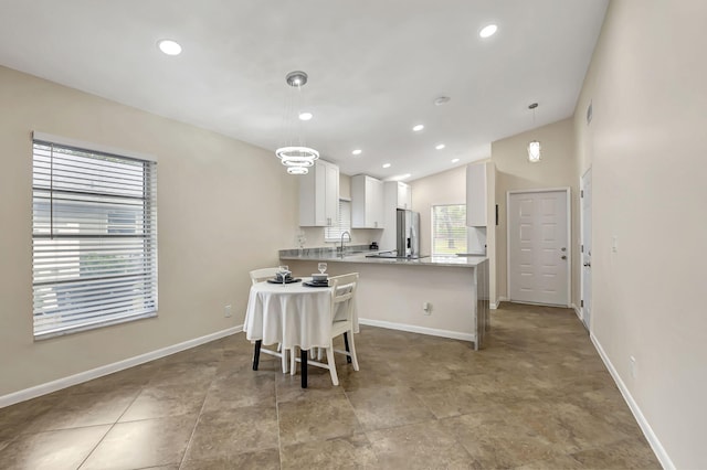 kitchen with kitchen peninsula, stainless steel refrigerator with ice dispenser, sink, decorative light fixtures, and white cabinets