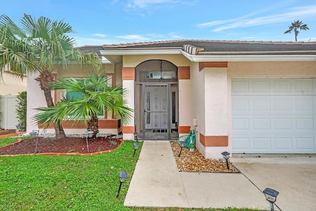 entrance to property featuring an attached garage, a lawn, and stucco siding