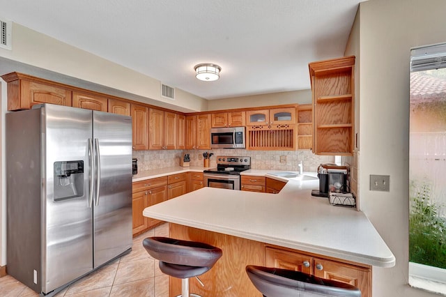 kitchen featuring light tile patterned floors, stainless steel appliances, tasteful backsplash, a kitchen bar, and kitchen peninsula