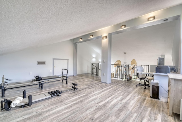 workout room featuring light wood-type flooring and a textured ceiling