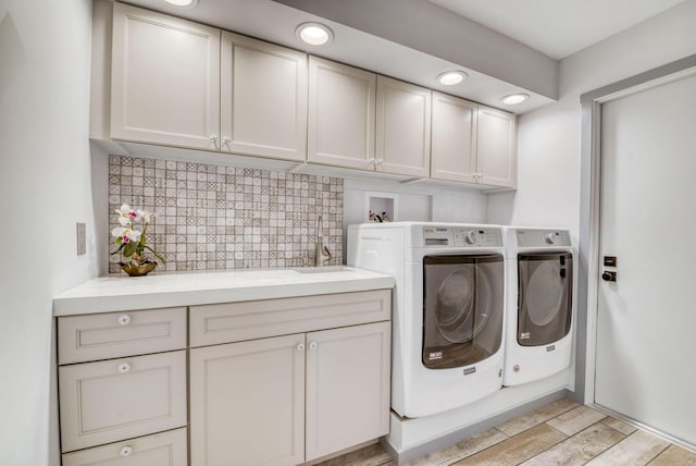 washroom with cabinets, washing machine and dryer, and light hardwood / wood-style flooring