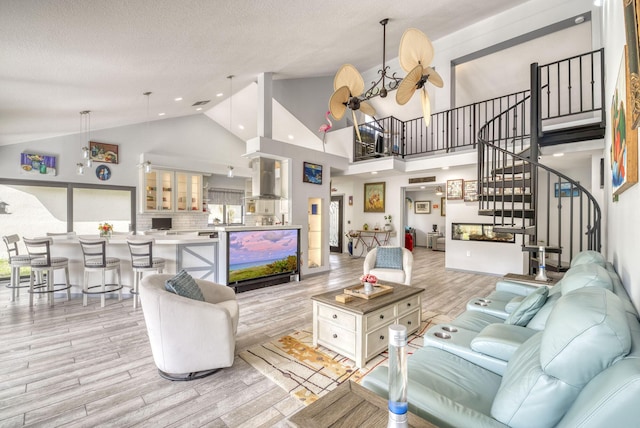 living room with ceiling fan, high vaulted ceiling, a textured ceiling, and light wood-type flooring