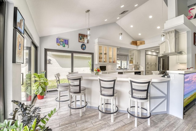 kitchen featuring high vaulted ceiling, decorative backsplash, decorative light fixtures, light hardwood / wood-style floors, and island exhaust hood