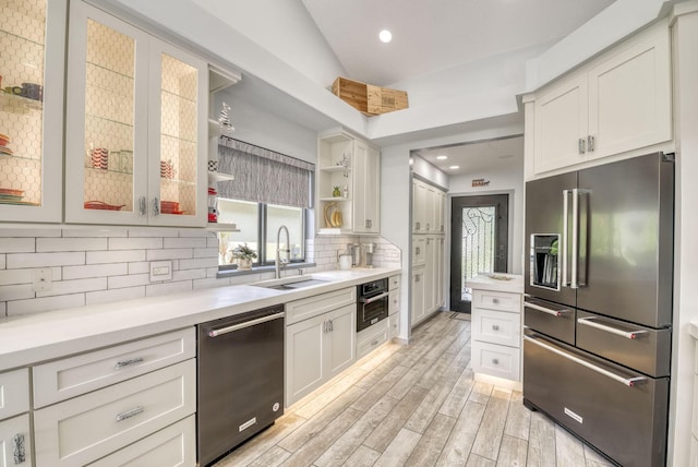 kitchen with appliances with stainless steel finishes, vaulted ceiling, decorative backsplash, white cabinets, and light wood-type flooring