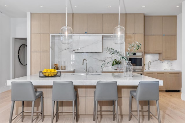 kitchen featuring hanging light fixtures, light wood-type flooring, sink, and a large island with sink