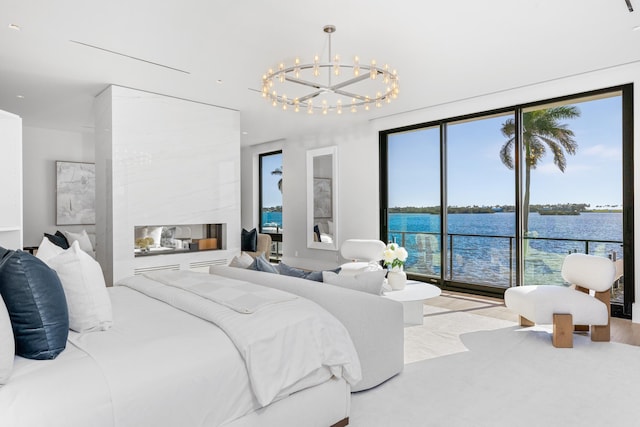 bedroom with a water view, a tiled fireplace, light hardwood / wood-style flooring, access to exterior, and a chandelier