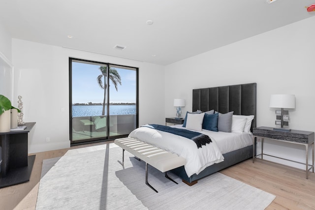 bedroom with access to exterior, light hardwood / wood-style flooring, and a water view