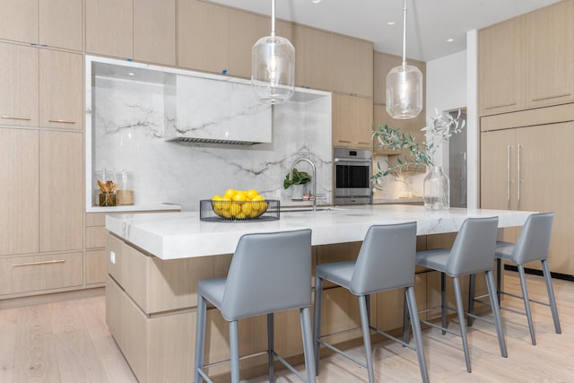 kitchen featuring light brown cabinetry, light hardwood / wood-style flooring, stainless steel oven, and a spacious island