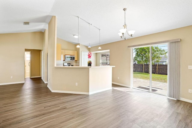 kitchen featuring stainless steel appliances, wood-type flooring, light brown cabinets, hanging light fixtures, and lofted ceiling