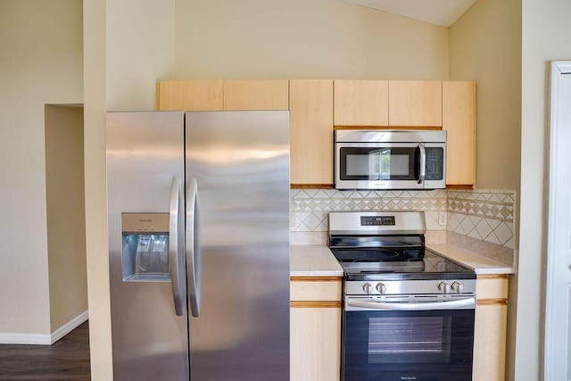 kitchen with vaulted ceiling, stainless steel appliances, light brown cabinetry, and tasteful backsplash