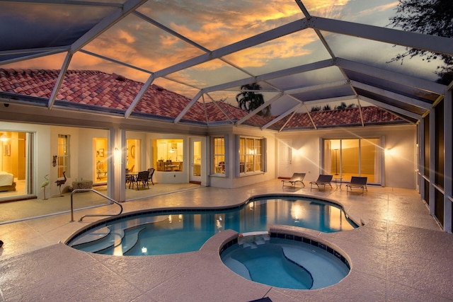 pool at dusk featuring a patio area, a lanai, and an in ground hot tub