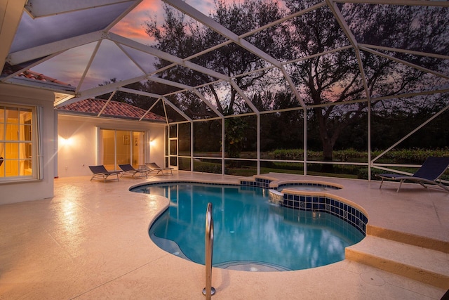 pool at dusk with a patio area, a lanai, and an in ground hot tub