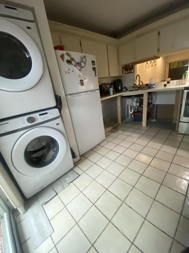 kitchen with white appliances, sink, cream cabinetry, stacked washer / drying machine, and light tile patterned flooring