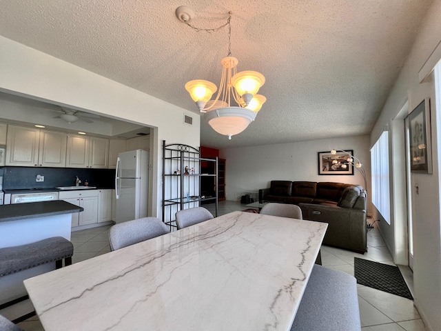 tiled dining area with ceiling fan with notable chandelier, a textured ceiling, and sink