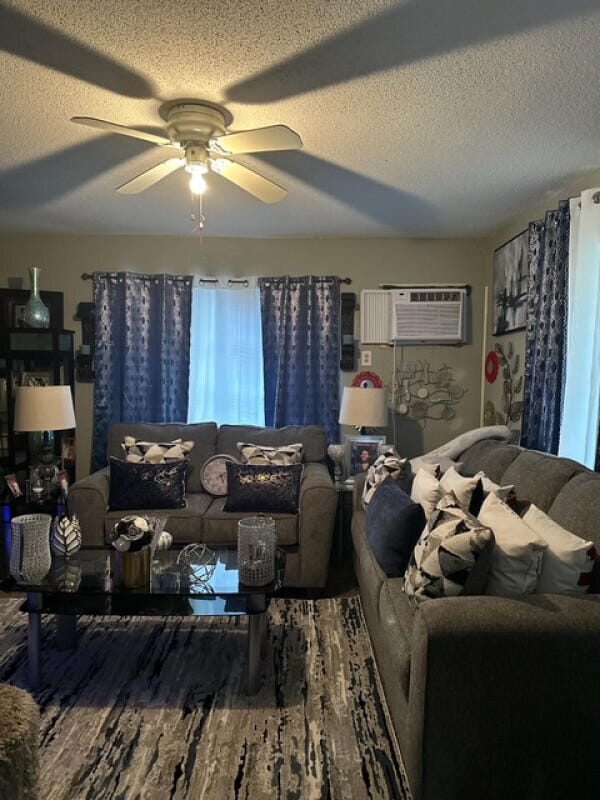 living room with a wall mounted air conditioner, ceiling fan, a textured ceiling, and hardwood / wood-style flooring