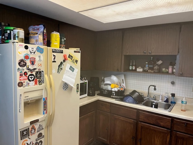 kitchen featuring dark brown cabinets, white appliances, sink, and tasteful backsplash