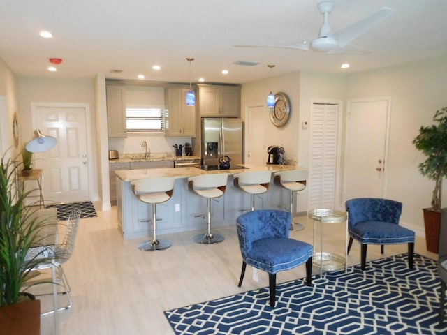 kitchen with a kitchen bar, stainless steel fridge, light wood-type flooring, gray cabinetry, and hanging light fixtures