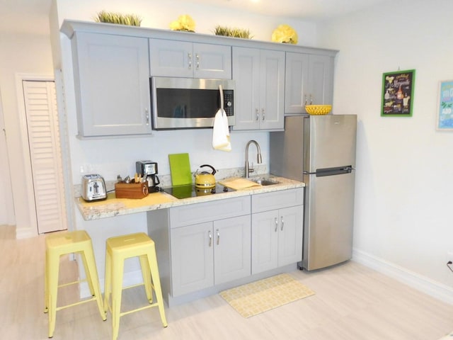 kitchen with a breakfast bar, sink, light stone countertops, light hardwood / wood-style floors, and stainless steel appliances