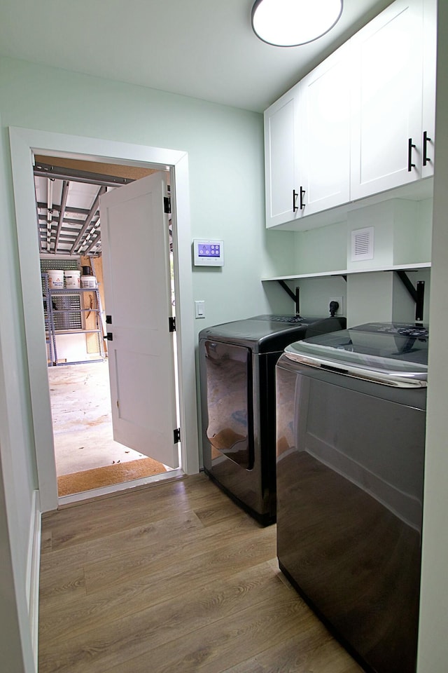 laundry room featuring washer and clothes dryer, light hardwood / wood-style floors, and cabinets