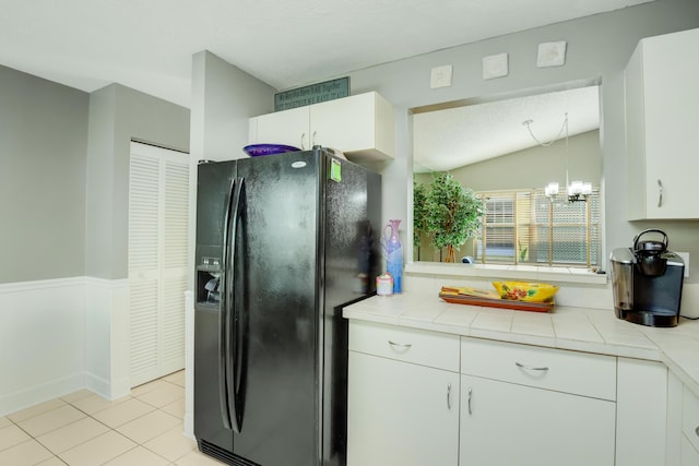 kitchen with tile countertops, white cabinets, black fridge, vaulted ceiling, and a notable chandelier