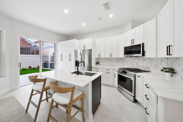 kitchen featuring white cabinets, a center island with sink, sink, appliances with stainless steel finishes, and light stone counters