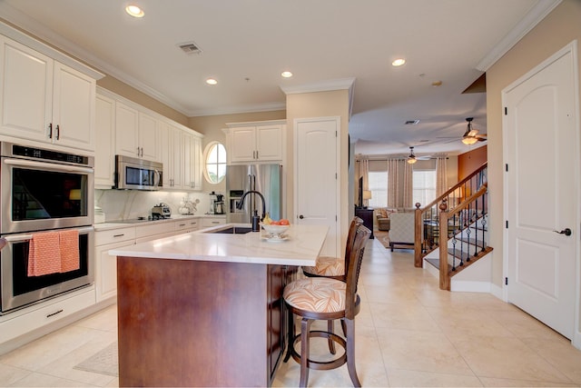 kitchen with ceiling fan, sink, a kitchen breakfast bar, a center island with sink, and appliances with stainless steel finishes