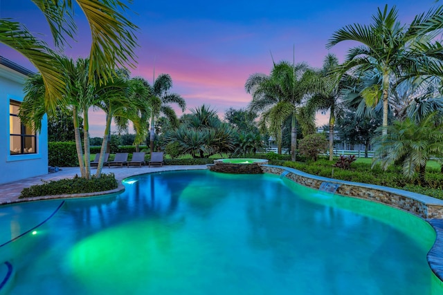 pool at dusk featuring an in ground hot tub and a patio area