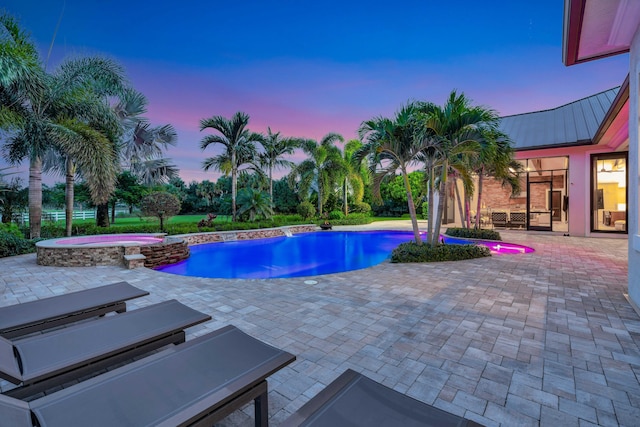 pool at dusk featuring a patio area and an in ground hot tub