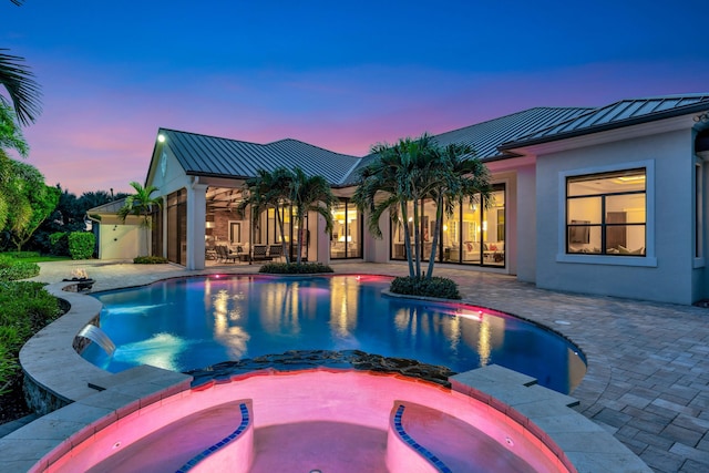 pool at dusk featuring a patio area and an in ground hot tub