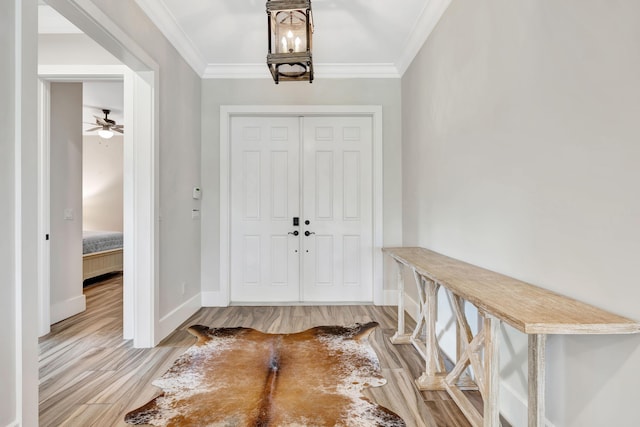 foyer entrance featuring crown molding, ceiling fan with notable chandelier, and light wood-type flooring