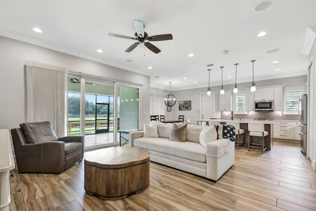 living room with ceiling fan with notable chandelier and ornamental molding