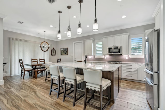 kitchen featuring a kitchen island with sink, white cabinetry, hanging light fixtures, and appliances with stainless steel finishes