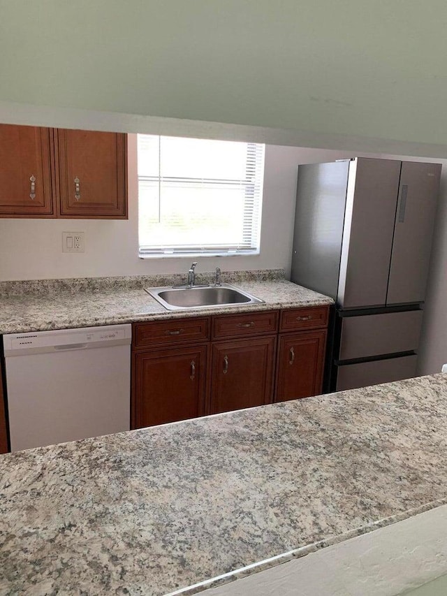 kitchen with stainless steel refrigerator, light stone countertops, dishwasher, and sink