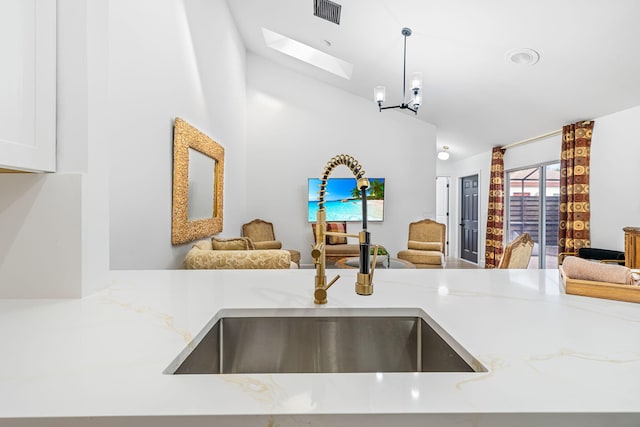 kitchen featuring sink, decorative light fixtures, a skylight, light stone countertops, and a notable chandelier