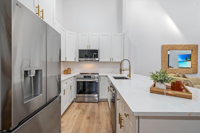 kitchen featuring white cabinets, appliances with stainless steel finishes, light stone counters, and sink