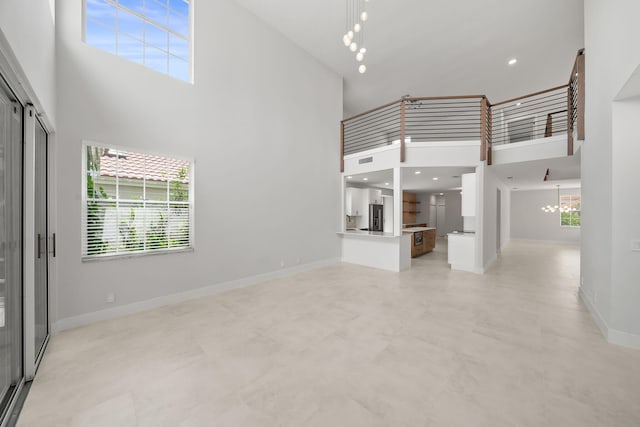 unfurnished living room with a notable chandelier, a towering ceiling, and a wealth of natural light