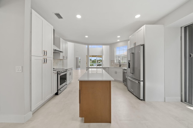 kitchen with kitchen peninsula, stainless steel appliances, sink, white cabinets, and a center island