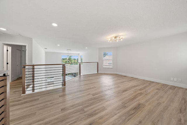 empty room featuring a textured ceiling, light wood-type flooring, and an inviting chandelier