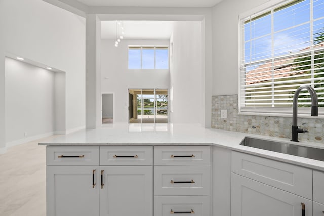 kitchen featuring backsplash, light stone counters, white cabinetry, and sink